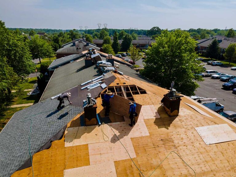 A homeowner examines a damp attic ceiling beneath stained roof decking and wet insulation.