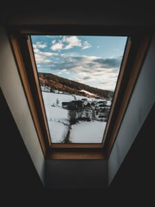 A residential roof skylight with metal flashing and light snow around the surrounding shingles.